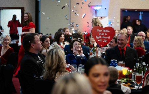 Silver confetti falling on a table of guests with a heart-shaped sign reading Our table has a full heart!